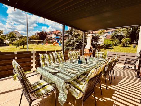 Große, überdachte Terrasse mit Grill und großem Tisch – ideal für gemeinsame Abende. Blick auf den Spielplatz im Garten, Kinder können spiel Große, überdachte Terrasse mit Grill und großem Tisch – ideal für gemeinsame Abende. Blick auf den Spielplatz im Garten, Kinder können spiel